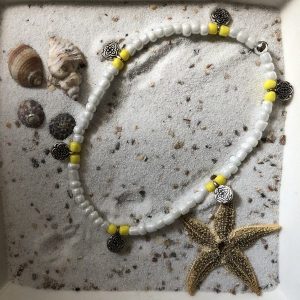 Enkelbandje (elastisch) van witte en gele kraaltjes met zilverkleurige muntjes