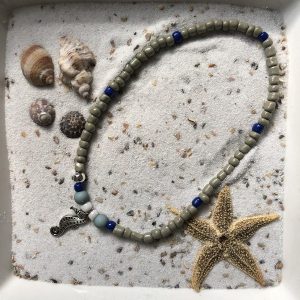 Enkelbandje (elastisch) van beige en donkerblauwe kraaltjes met zilverkleurige hanger "zeepaardje"